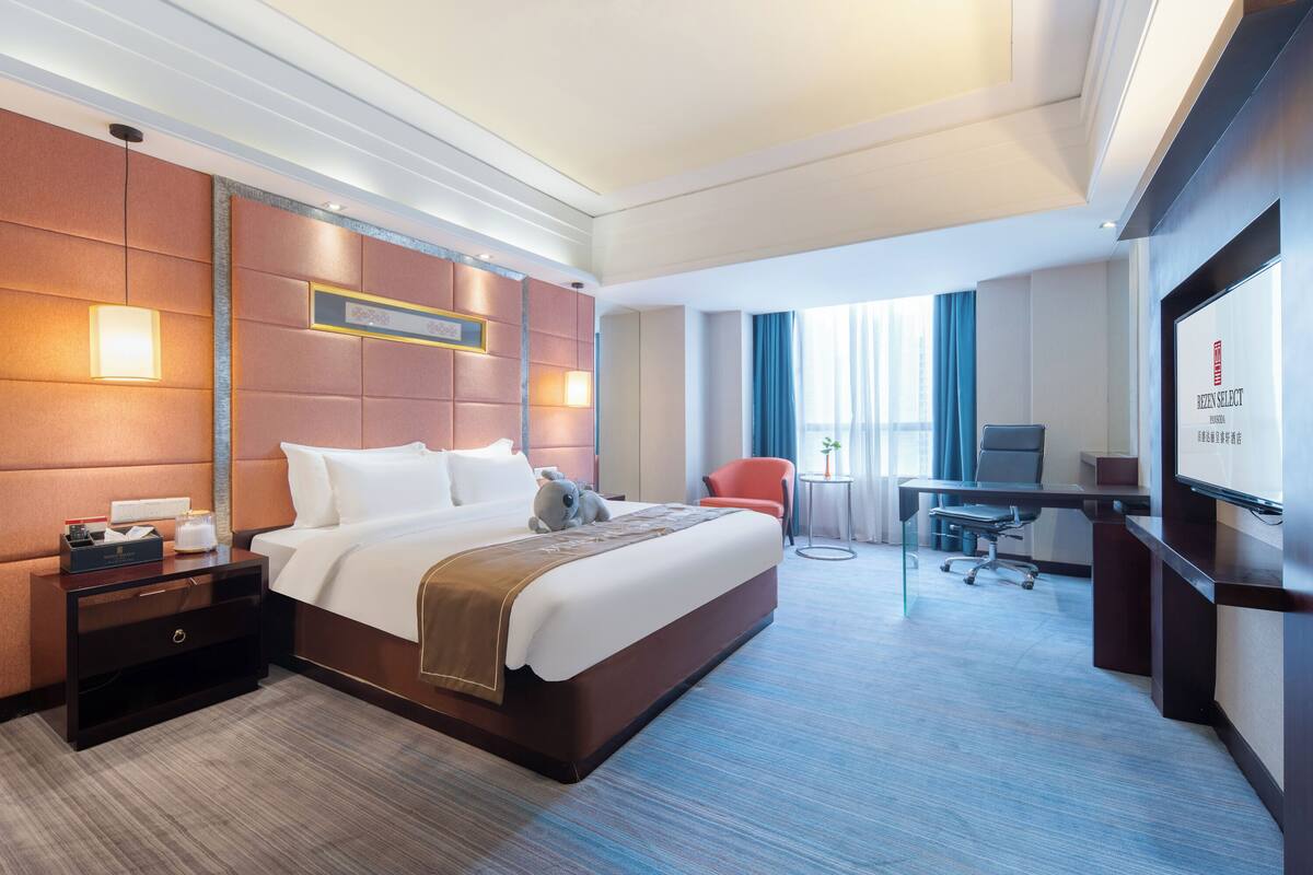 A hotel room with a large bed, a desk, and a television.