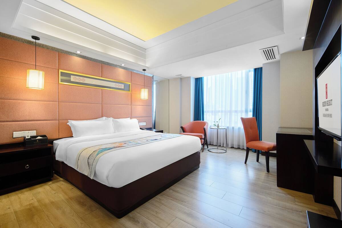 A hotel room with a large bed, a desk, a chair, and a TV.