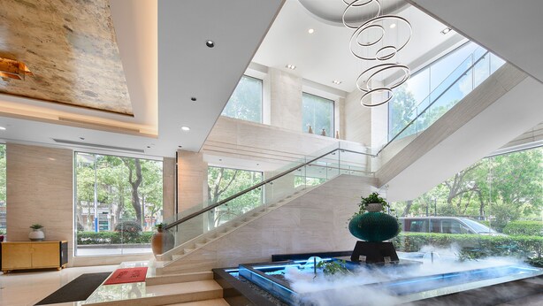 Eine moderne Lobby mit einer Glaswendeltreppe, einem Wasserspiel und Blick ins Freie.