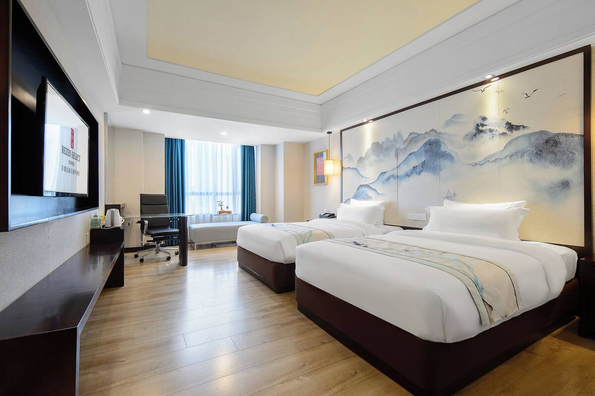 A hotel room with two beds, a desk, a chair, a TV, and a large painting on the wall.