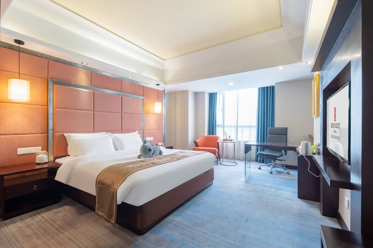 A hotel room with a large bed, a desk, a chair, a TV, and a window with curtains.