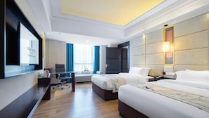 Ein Hotelzimmer mit zwei Betten, einem Schreibtisch, einem Fernseher und einem großen Fenster mit Vorhängen.
