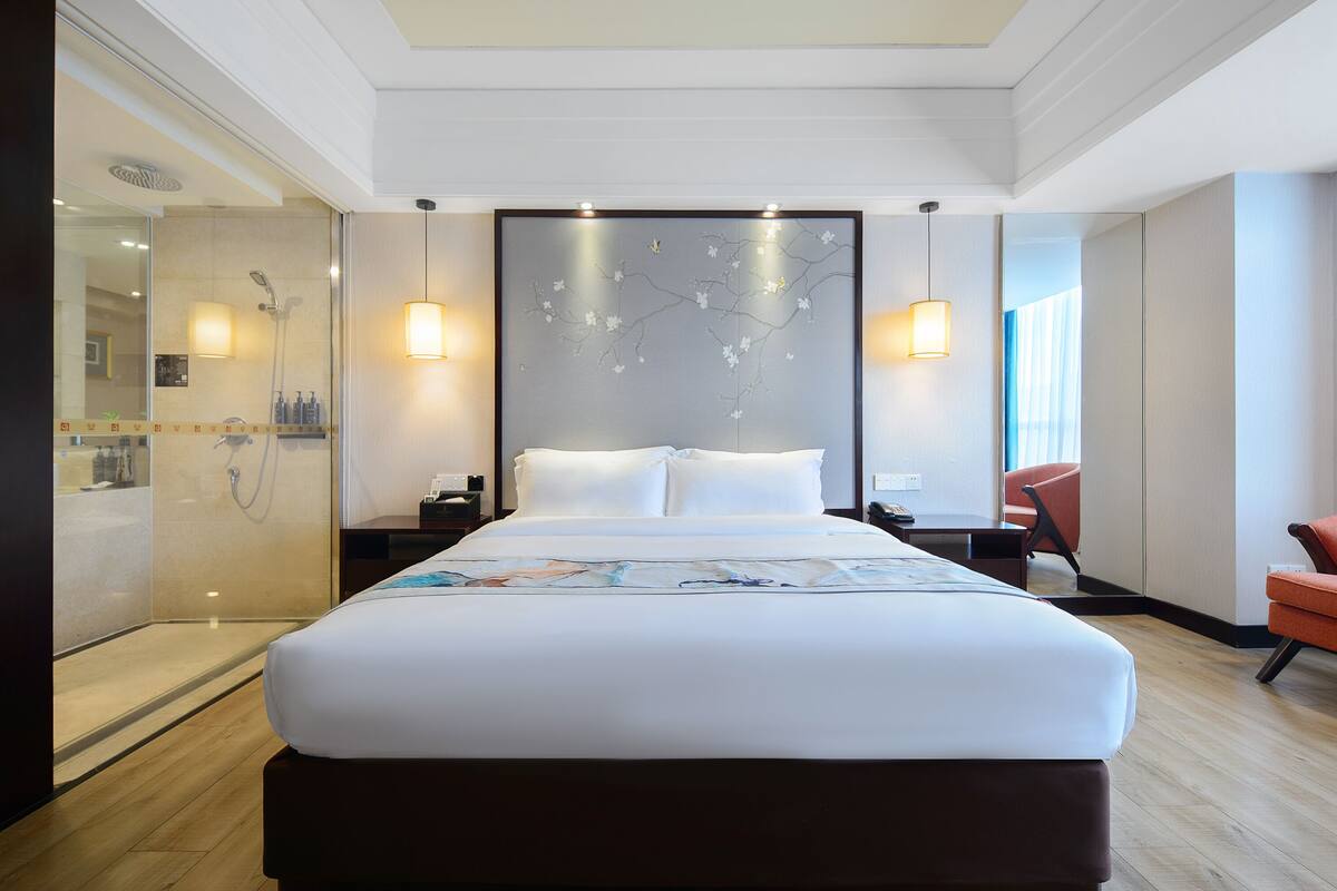 A modern hotel room with a large bed, a glass shower enclosure, and two bedside lamps.