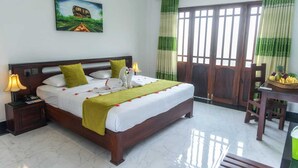 Quarto de hotel com uma cama grande, mesa de cabeceira, escrivaninha com uma cesta de frutas e um quadro na parede.