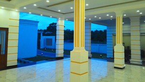 Um hall de entrada com piso de mármore, colunas brancas com listras amarelas e luminárias embutidas no teto.