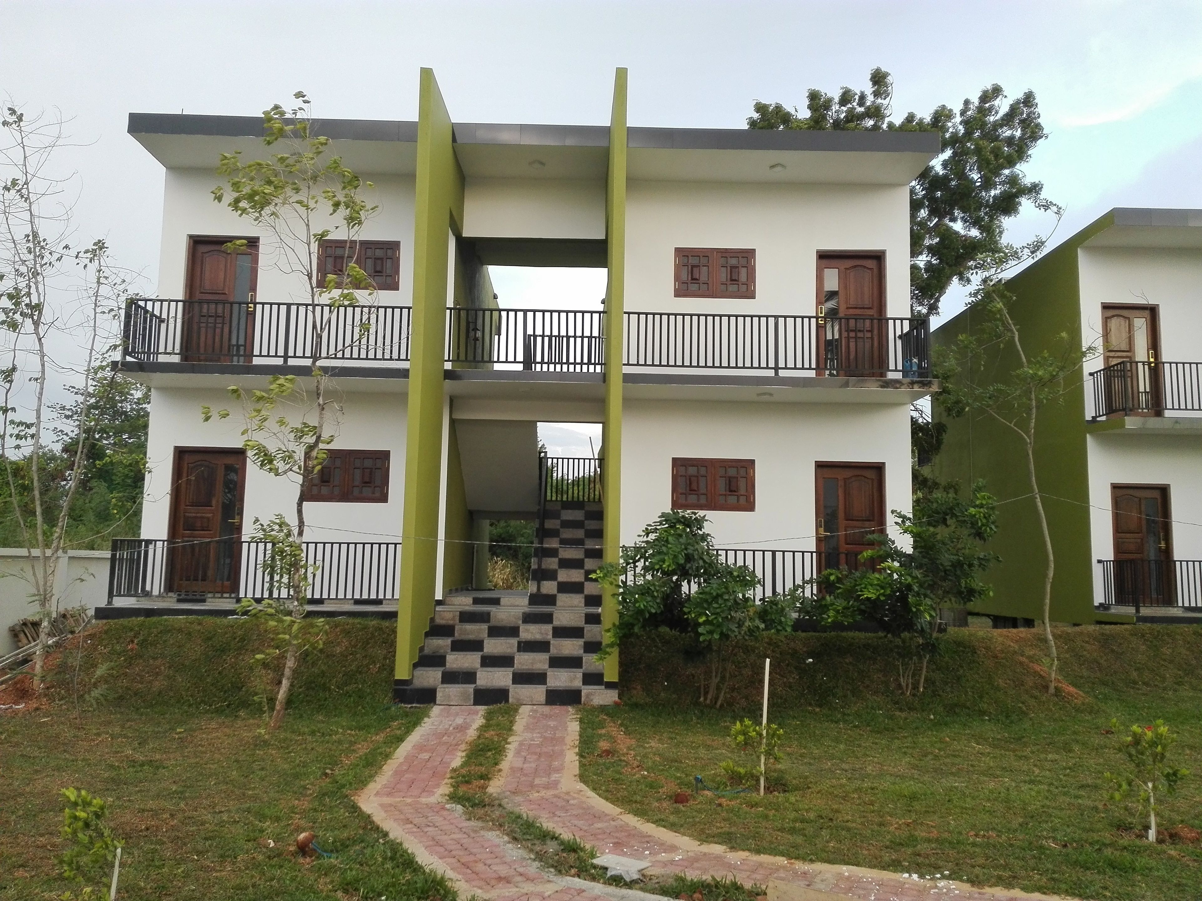 A two-story building with a central staircase, balconies, and a checkered pathway leading to the entrance.