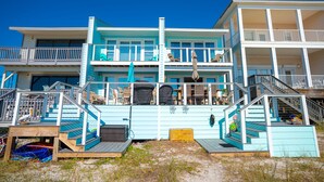 Una propiedad frente a la playa con varios pisos, balcones, asientos al aire libre y una terraza de madera.