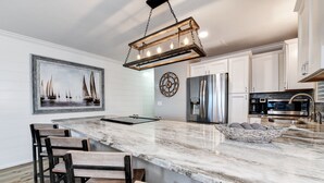 Una cocina con una isla grande, armarios blancos, electrodomésticos de acero inoxidable y una lámpara colgante.