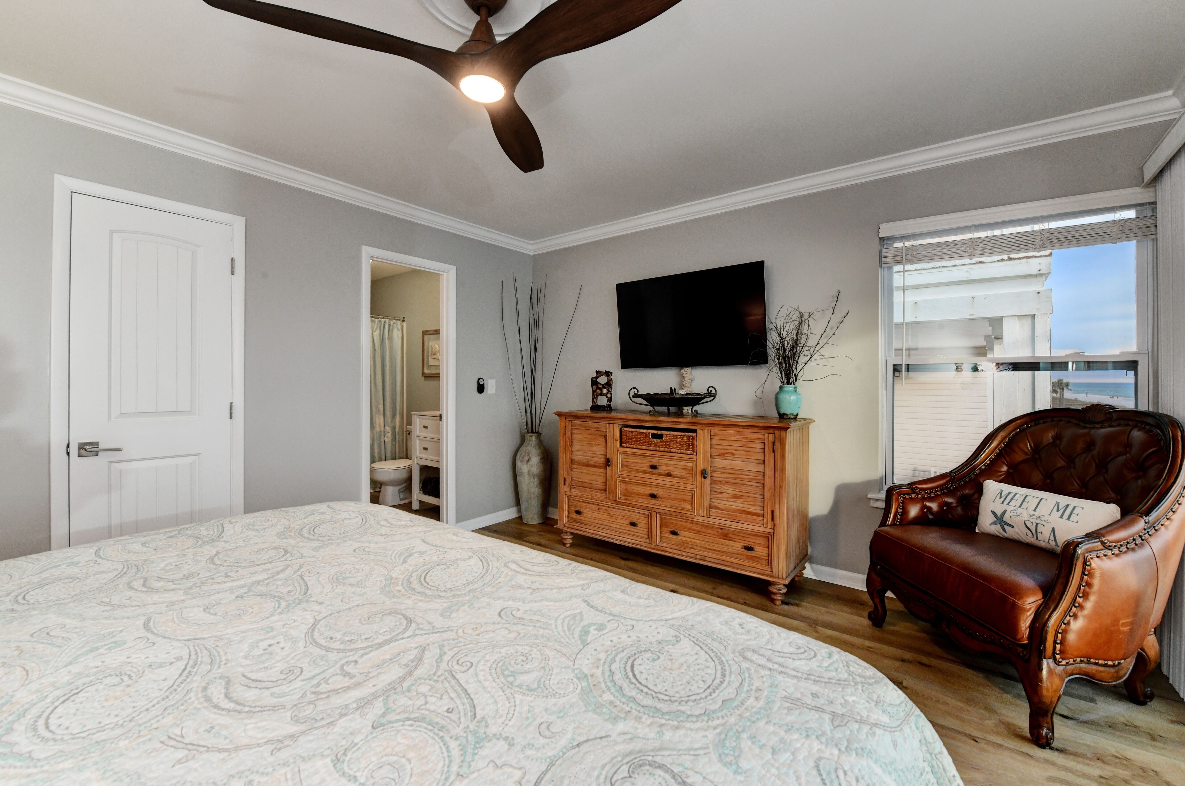 A bedroom with a large bed, a wooden dresser, a television, and a window with a view.