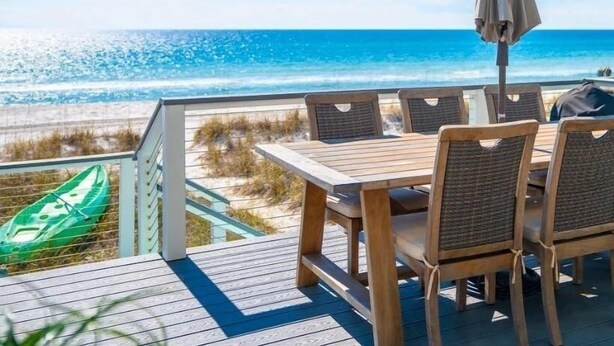 Una terraza de madera con una mesa y sillas que dan al océano.