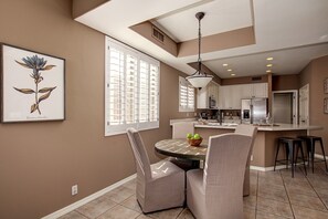 A modern kitchen with white cabinets, a stainless steel refrigerator, and a dining area with a round table and chairs.