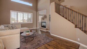 A spacious living room with a sofa, coffee table, and a fireplace. A staircase with a wooden railing leads to an upper level. - Beautiful Golf Course with Pool &  Mountain views! (Glendale)