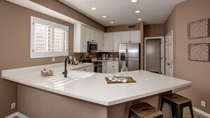 A modern kitchen with white cabinetry, a large island, stainless steel appliances, and a window with blinds. - Beautiful Golf Course with Pool &  Mountain views! (Glendale)