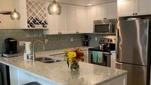 A modern kitchen with white cabinetry, a stainless steel refrigerator, a microwave, and a large island with bar stools. - Newly Renovated kitchen, guest and master bathrooms (Clearwater)