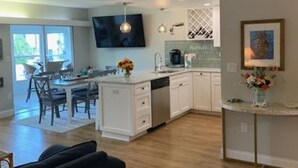 A modern kitchen with white cabinets, a dishwasher, and a dining area with a table and chairs. - Newly Renovated kitchen, guest and master bathrooms (Clearwater)