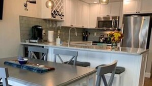 A modern kitchen with white cabinets, a stainless steel refrigerator, and a dining area with a table and chairs. - Newly Renovated kitchen, guest and master bathrooms (Clearwater)
