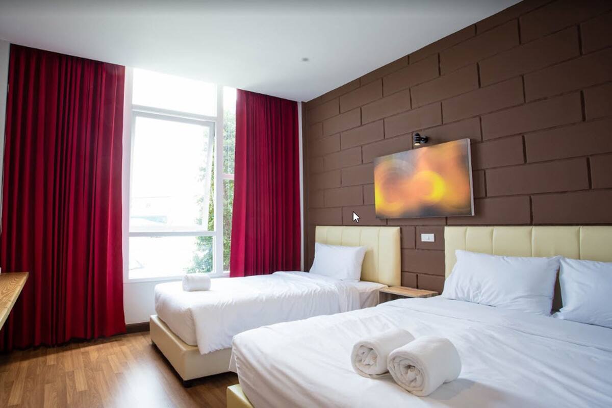 Een hotelkamer met twee bedden, rode gordijnen, een groot raam en een schilderij aan de muur.