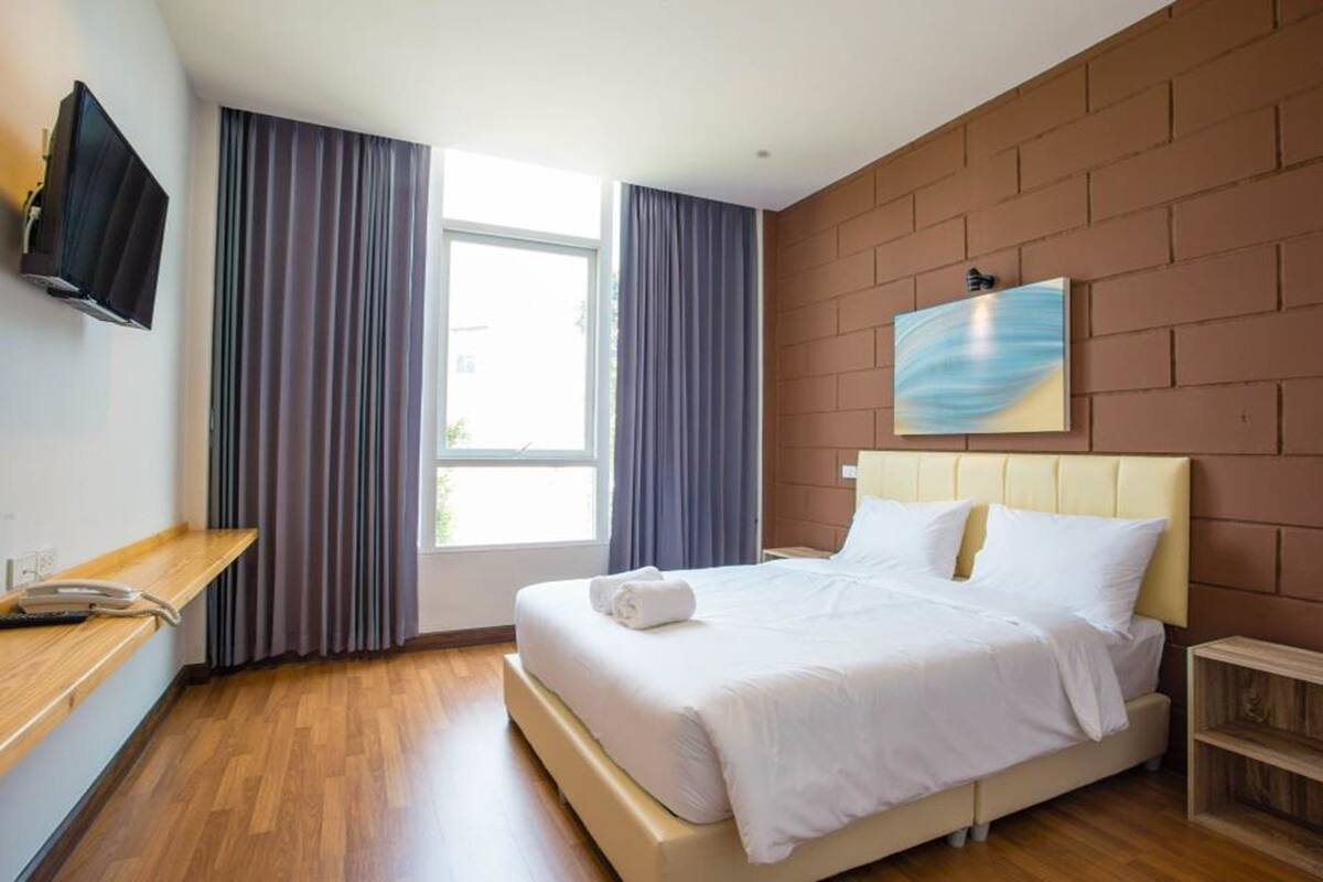 Een hotelkamer met een bed, een aan de muur bevestigde televisie, een raam met gordijnen en een houten vloer.