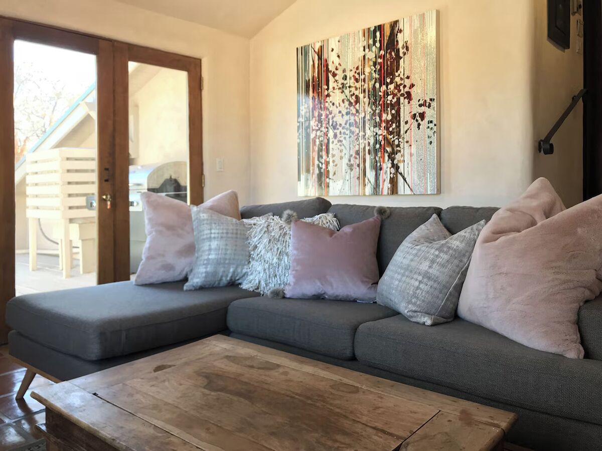Ein modernes Wohnzimmer mit einem grauen Ecksofa, einem Couchtisch aus Holz und einem großen abstrakten Gemälde an der Wand.