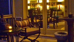 A dining area with a glass partition, cushioned chairs, a small table with a candle, and a stone planter.