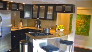 A modern kitchen with dark cabinets, a stainless steel refrigerator, a gas stove, and a small island with bar stools.