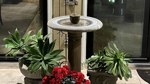 A stone fountain with candles, surrounded by potted plants and a decorative wall.
