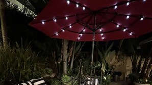 An outdoor seating area with a glass-top table, striped cushions, and a red umbrella.