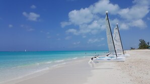 Ein Strand mit weißem Sand und türkisblauem Wasser. Segelboote liegen an der Küste vor Anker.