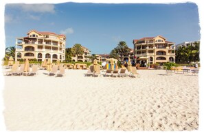 A beachfront hotel with multiple balconies, sun loungers, and palm trees.