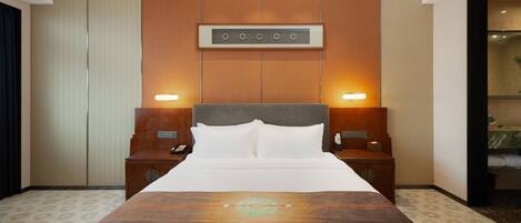 Una habitación de hotel con una cama grande, dos mesitas de noche, un panel de control en la pared y un baño visible a través de una puerta abierta.