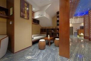 Un moderno hall de hotel con un sofá, estanterías de madera, una mesita y un separador decorativo.