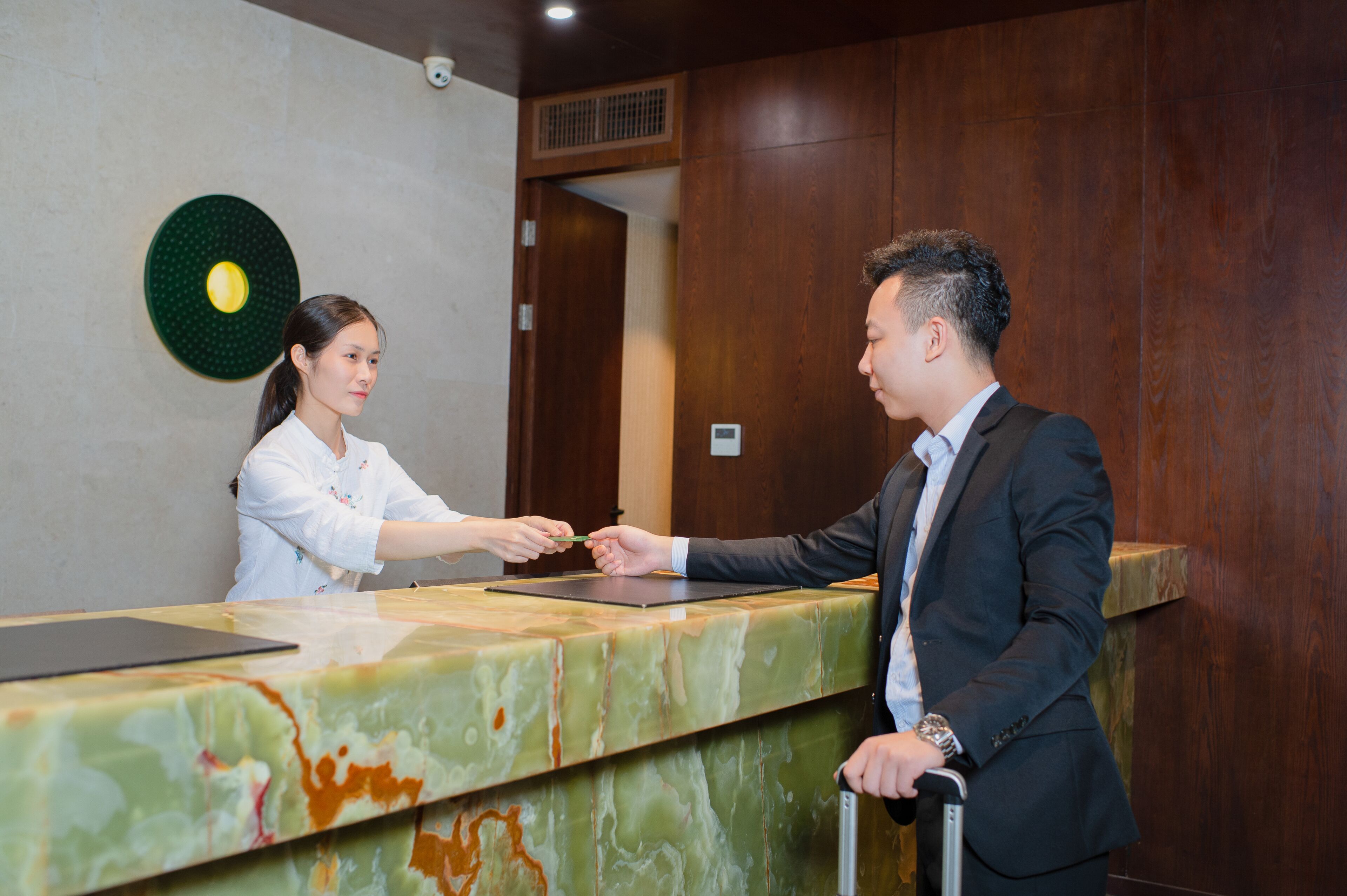 A reception desk with a marble top, a digital screen, and a green wall decoration.