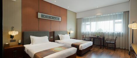 A hotel room with two beds, a desk, a chair, and a large window with curtains.