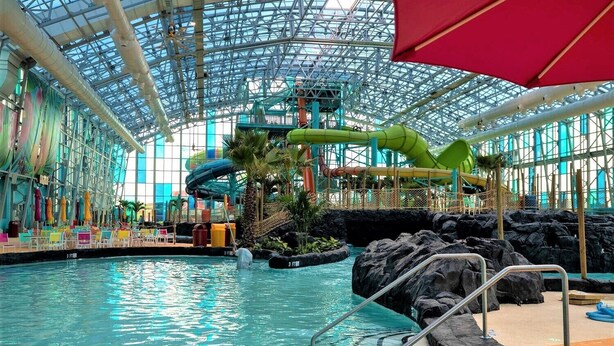 Parque acuático interior con una piscina grande, toboganes y techo de cristal.