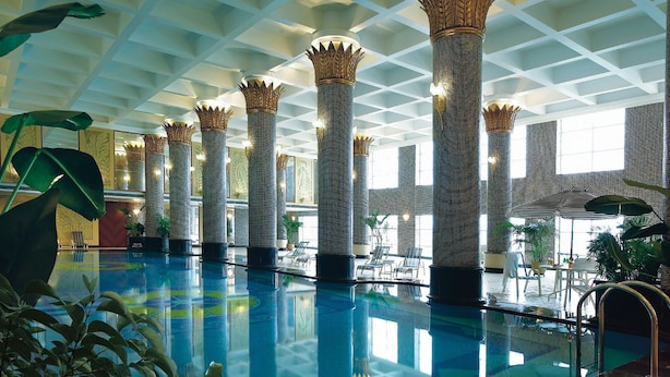 An indoor swimming pool with tall columns, lounge chairs, and potted plants. - Regal Palace Hotel  (Dongguan)