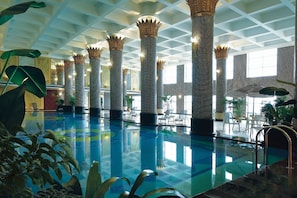 Una piscina interior con altas columnas, sillones de descanso y plantas en macetas.