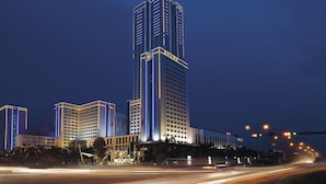 A high-rise hotel with multiple floors, illuminated by vertical lighting strips, and surrounded by other buildings. - Regal Palace Hotel  (Dongguan)