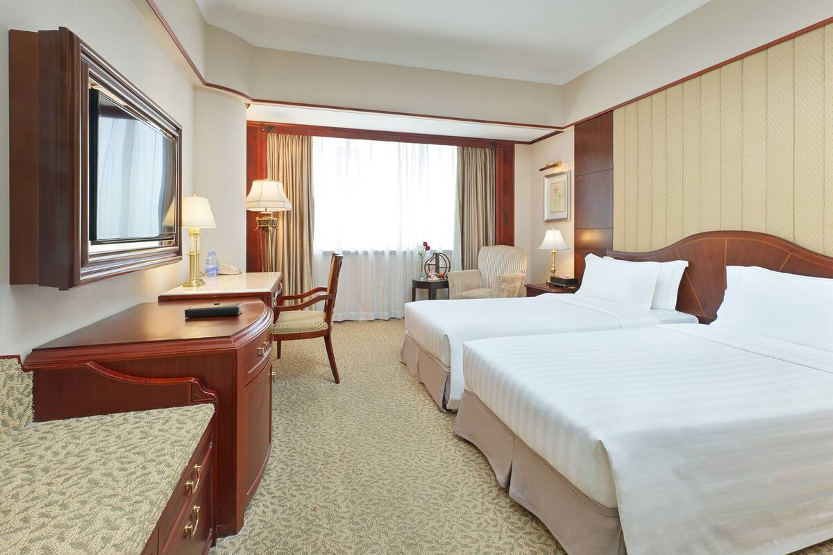 A hotel room with a large bed, a desk, a chair, a lamp, and a window with curtains.