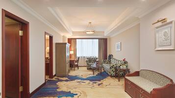 Habitación de hotel con un ventanal grande, un sofá, una silla, una mesita y piso alfombrado.