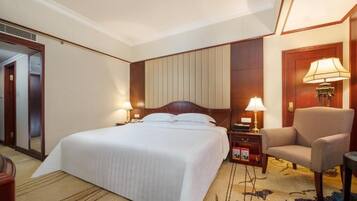 Una habitación de hotel con una cama grande, dos mesitas de noche con lámparas, una silla y piso alfombrado.