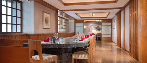 A long dining table with chairs, a chandelier, wooden paneling, and artwork on the walls.