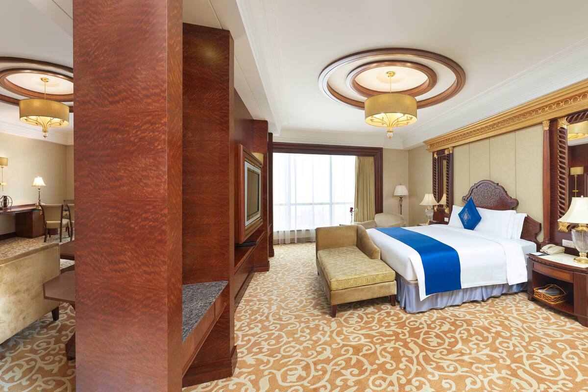 A hotel room with a large bed, a desk with a television, a chair, and a large mirror.