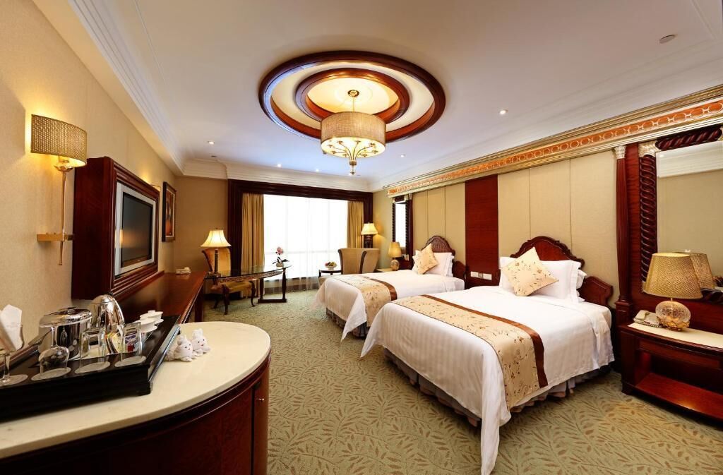 Quarto de hotel com duas camas, uma escrivaninha com bandeja de amenidades, um espelho grande e um candelabro.