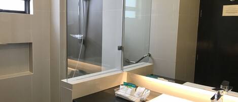 A modern bathroom with a large mirror, a white sink, a black countertop, and a glass shower enclosure.