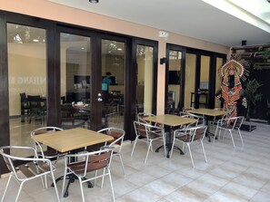 Un espace extérieur aménagé avec des tables et des chaises, une entrée avec une porte vitrée et un élément décoratif mural.