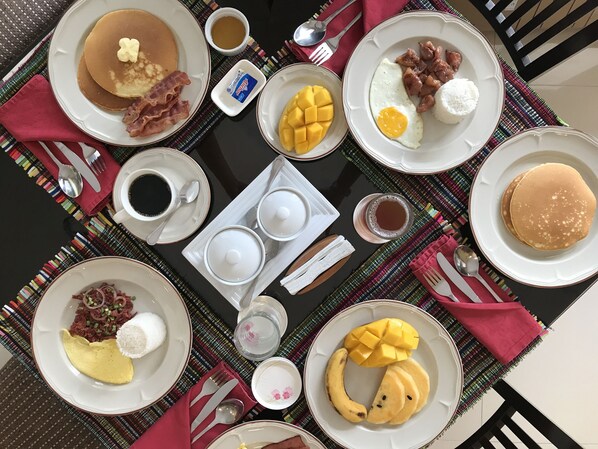 A breakfast table with various dishes including pancakes, eggs, bacon, and fruit.
