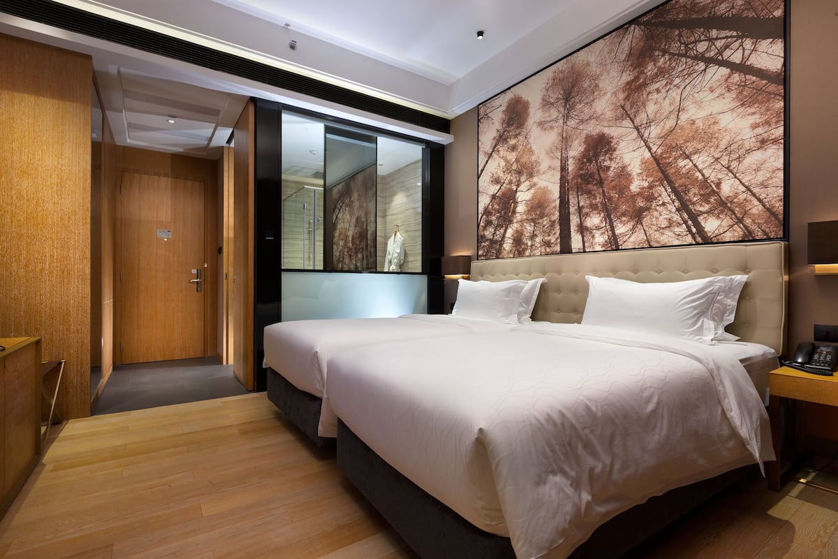 Une chambre d’hôtel avec un grand lit, une armoire, un miroir et une grande fenêtre donnant sur des arbres.