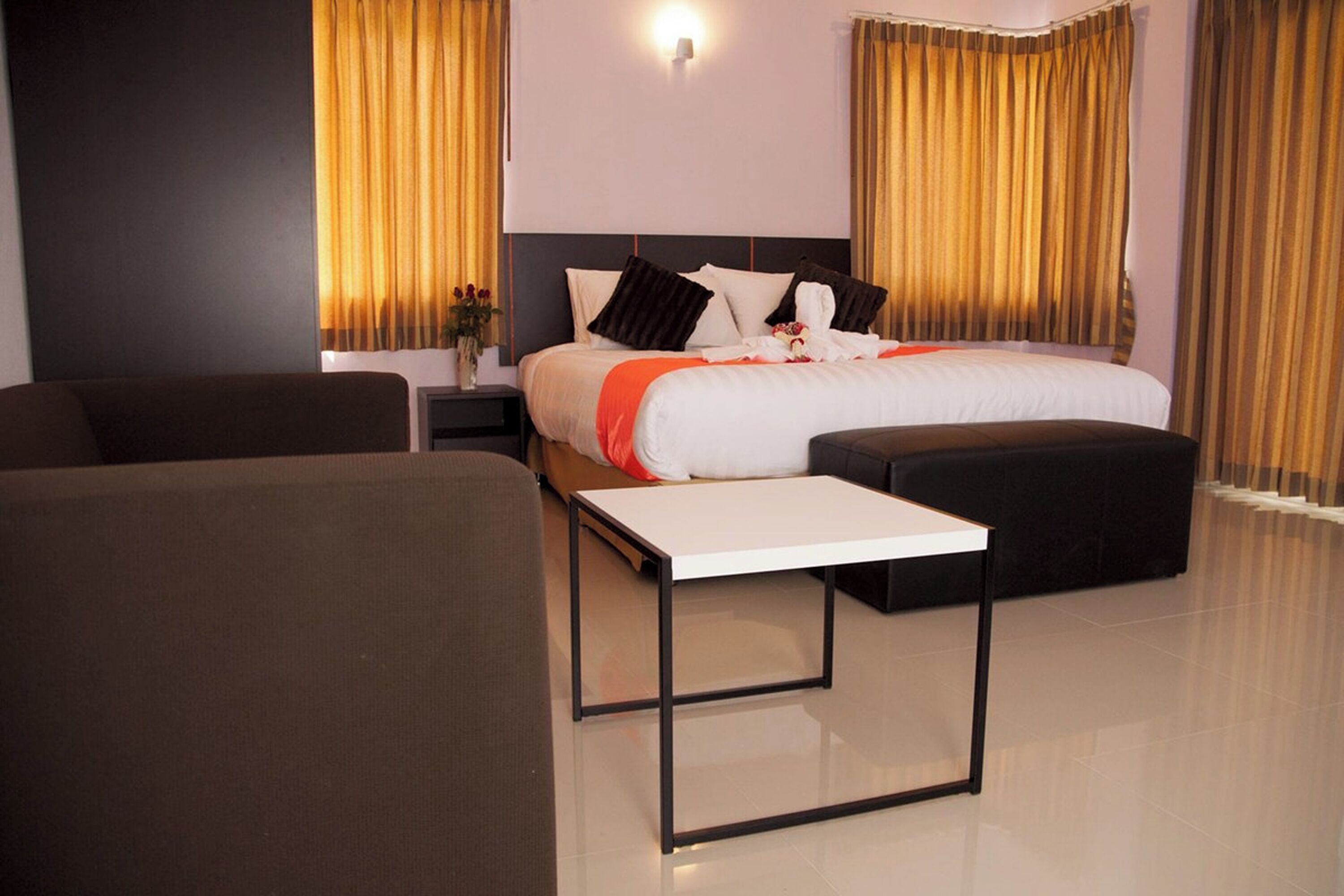 A modern hotel room with a large bed, a sofa, a small table, and a nightstand.