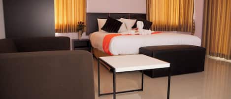 A modern hotel room with a large bed, a sofa, a small table, and a nightstand.