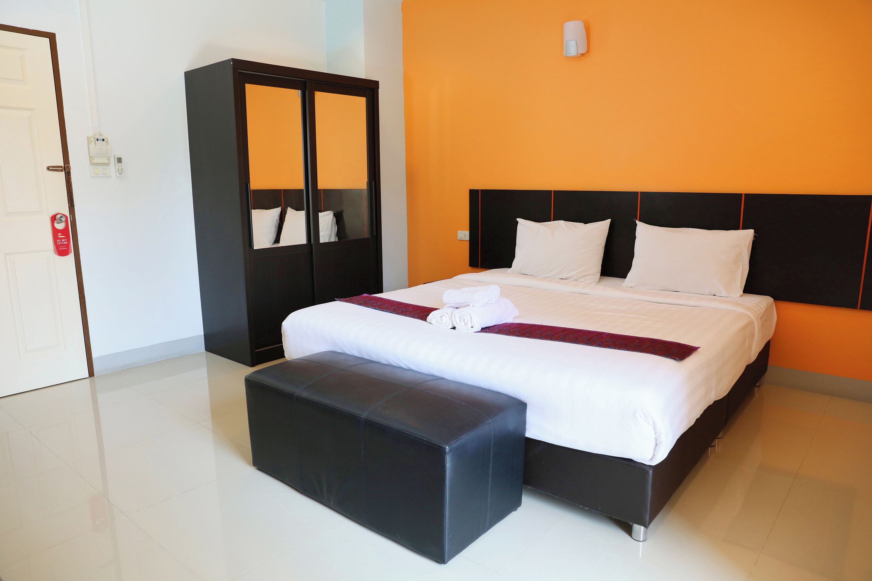 A hotel room with a bed, a bench, a wardrobe, and a door.